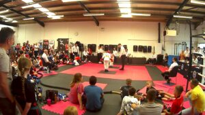 Black and red mats with two people in sparring kits surrounded by people watching
